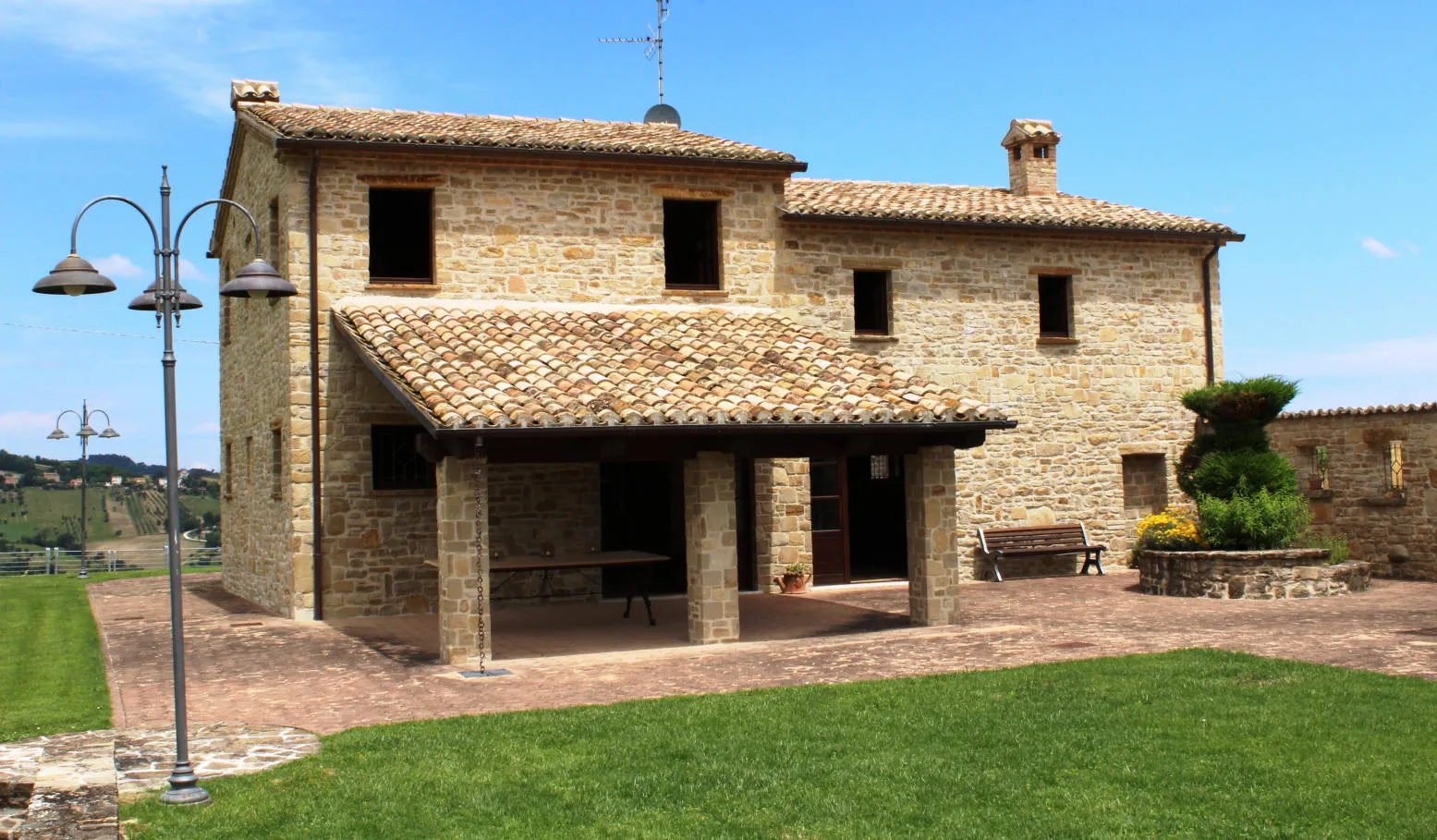 Un casale in pietra con il portico, il prato e le colline dietro