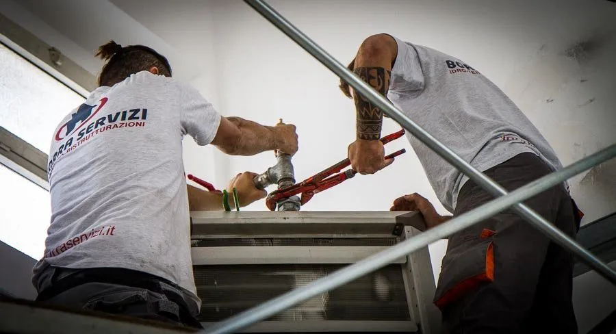 Due idraulici al lavoro su un impianto, con la maglia dell'impresa