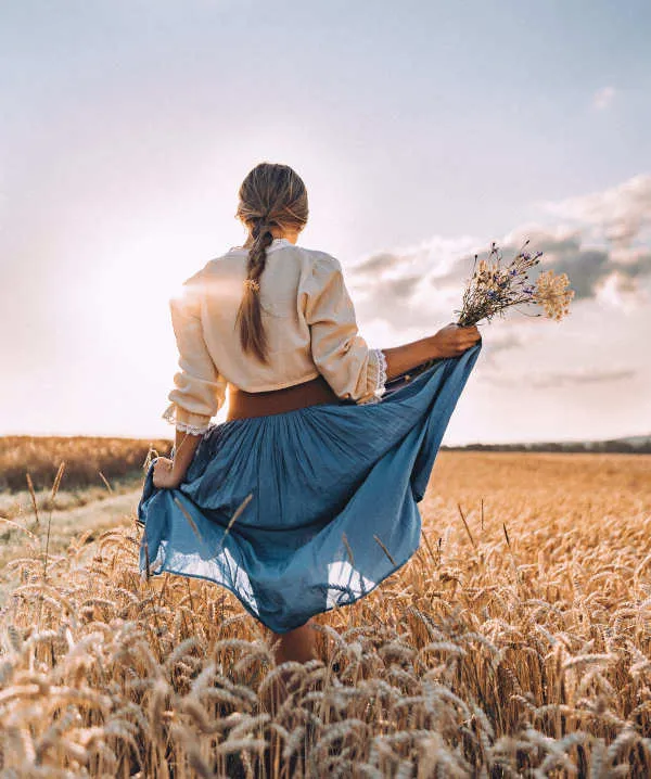 Una donna in un campo di grano, di spalle, con un mazzo di fiori