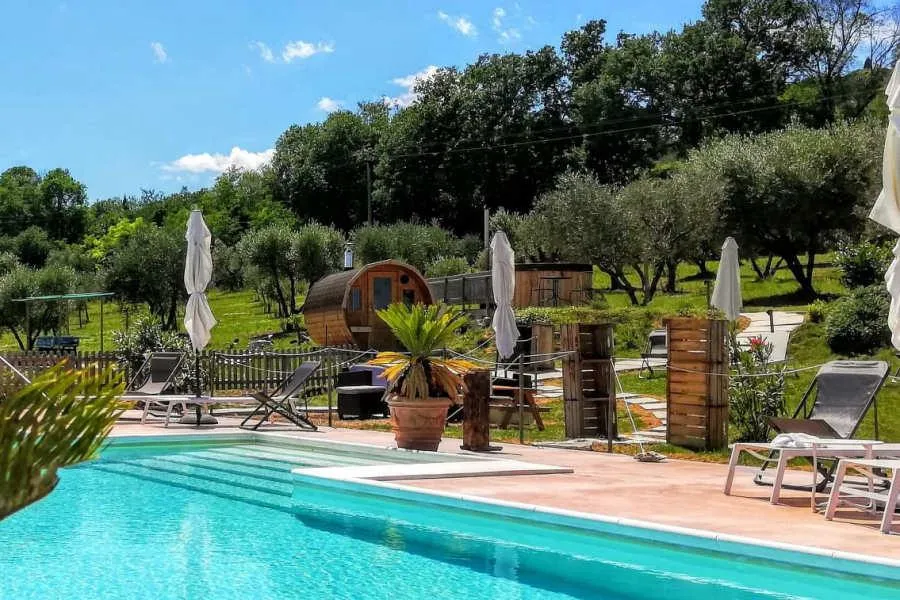Una piscina azzurra nel verde, con le sdraio e una botte-sauna in legno
