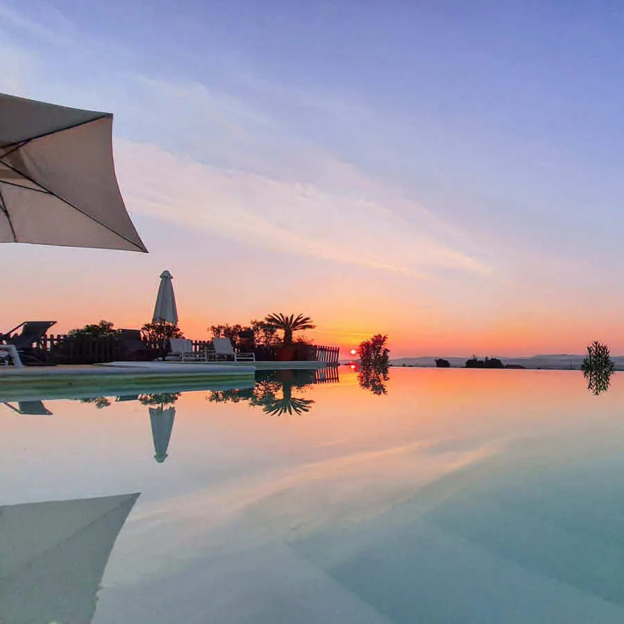 Il tramonto sull'acqua di una piscina a sfioro, con un ombrellone e le palme