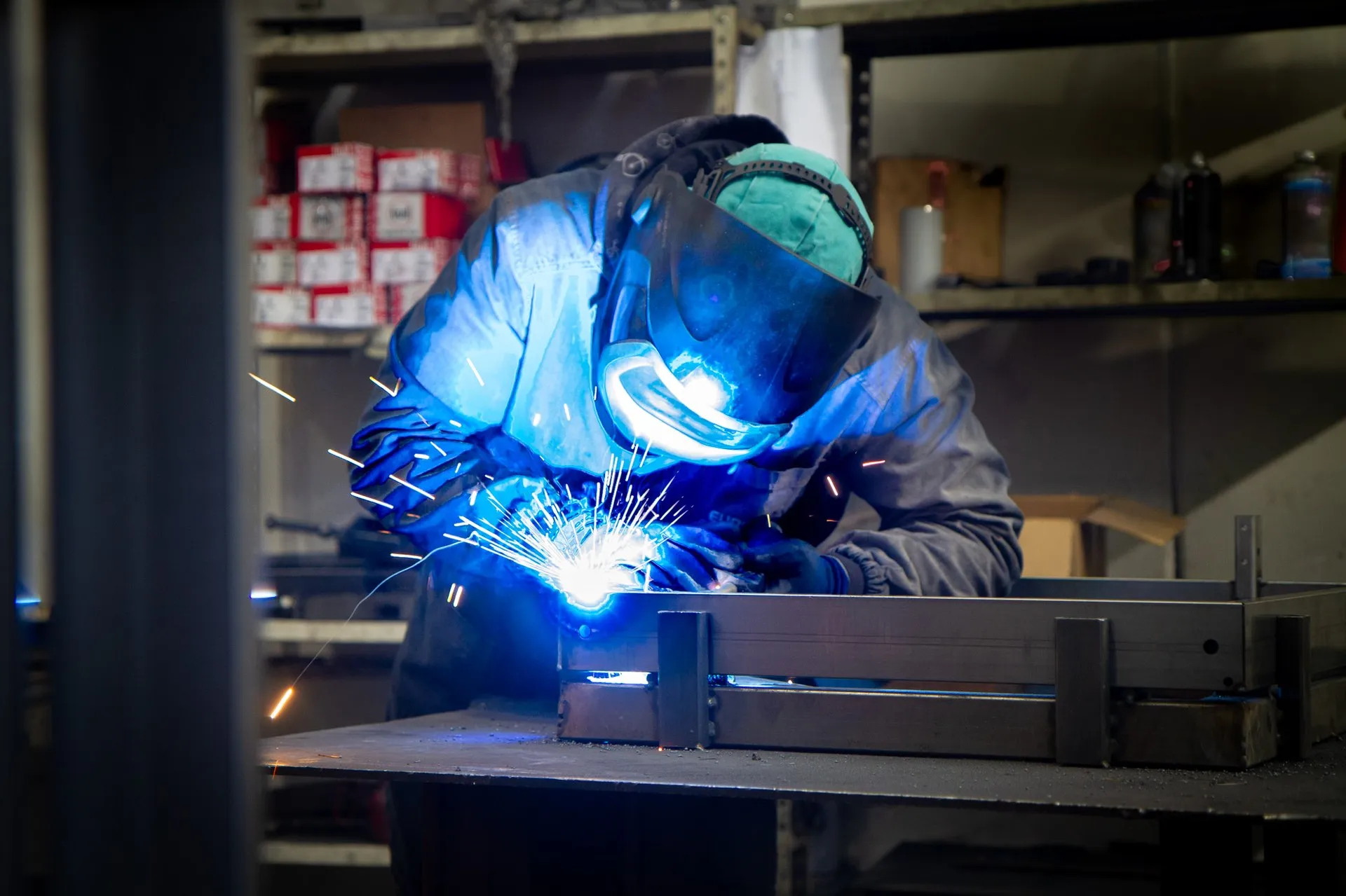 Un operaio che salda in officina, con le scintille e la luce blu