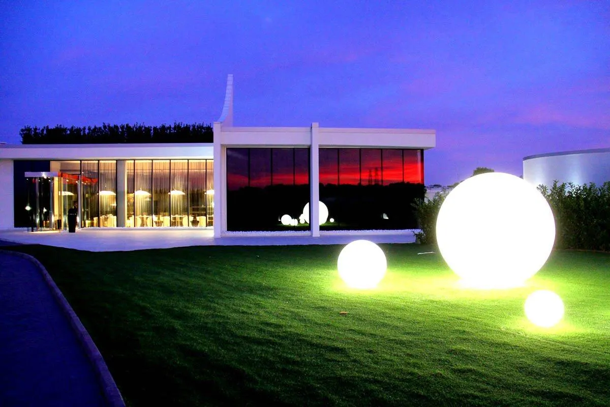 Un edificio illuminato di notte, con il prato e una sfera luminosa in primo piano